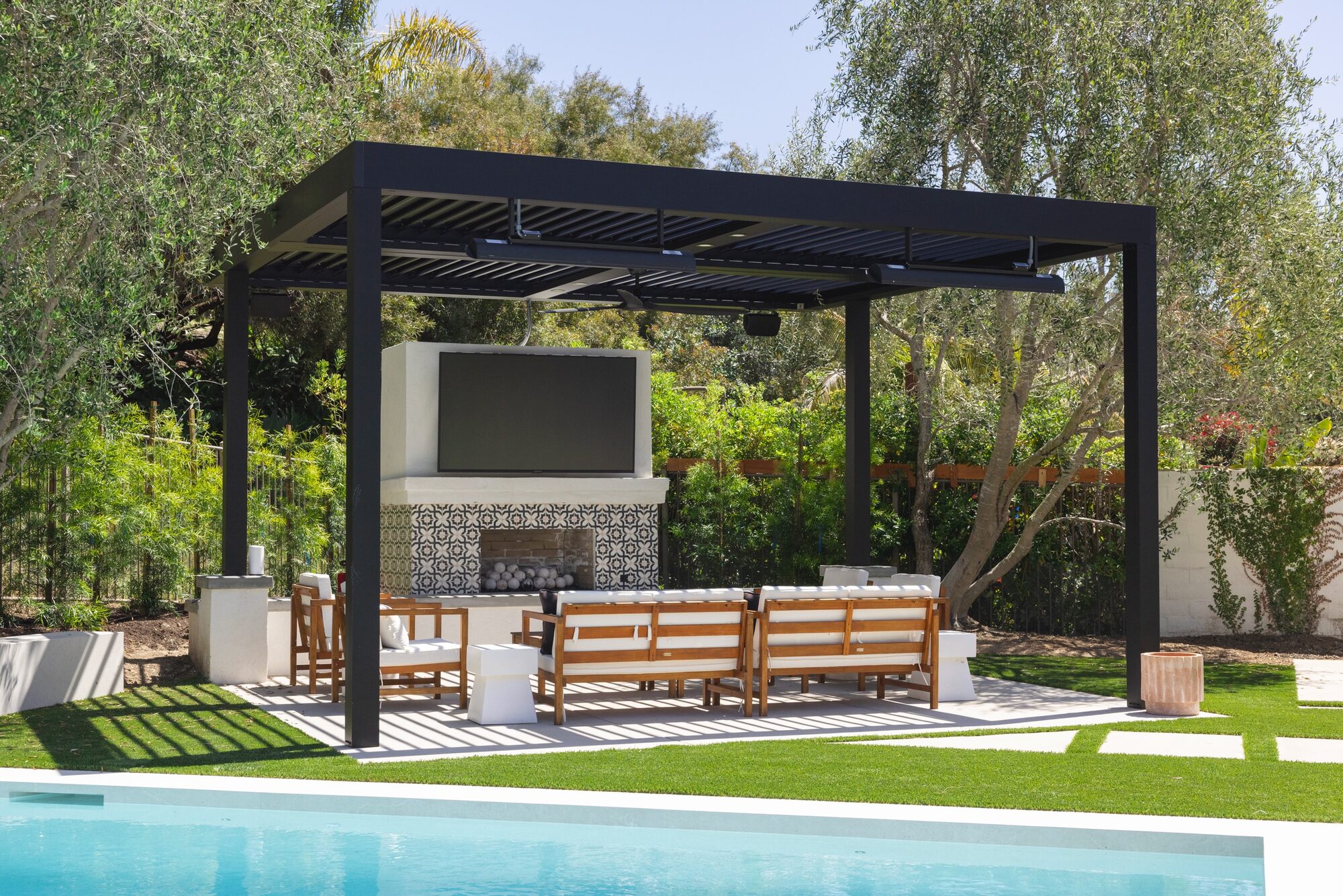 Covered pergola with TV wall, tile fireplace and teak seating — the Bespoke standard