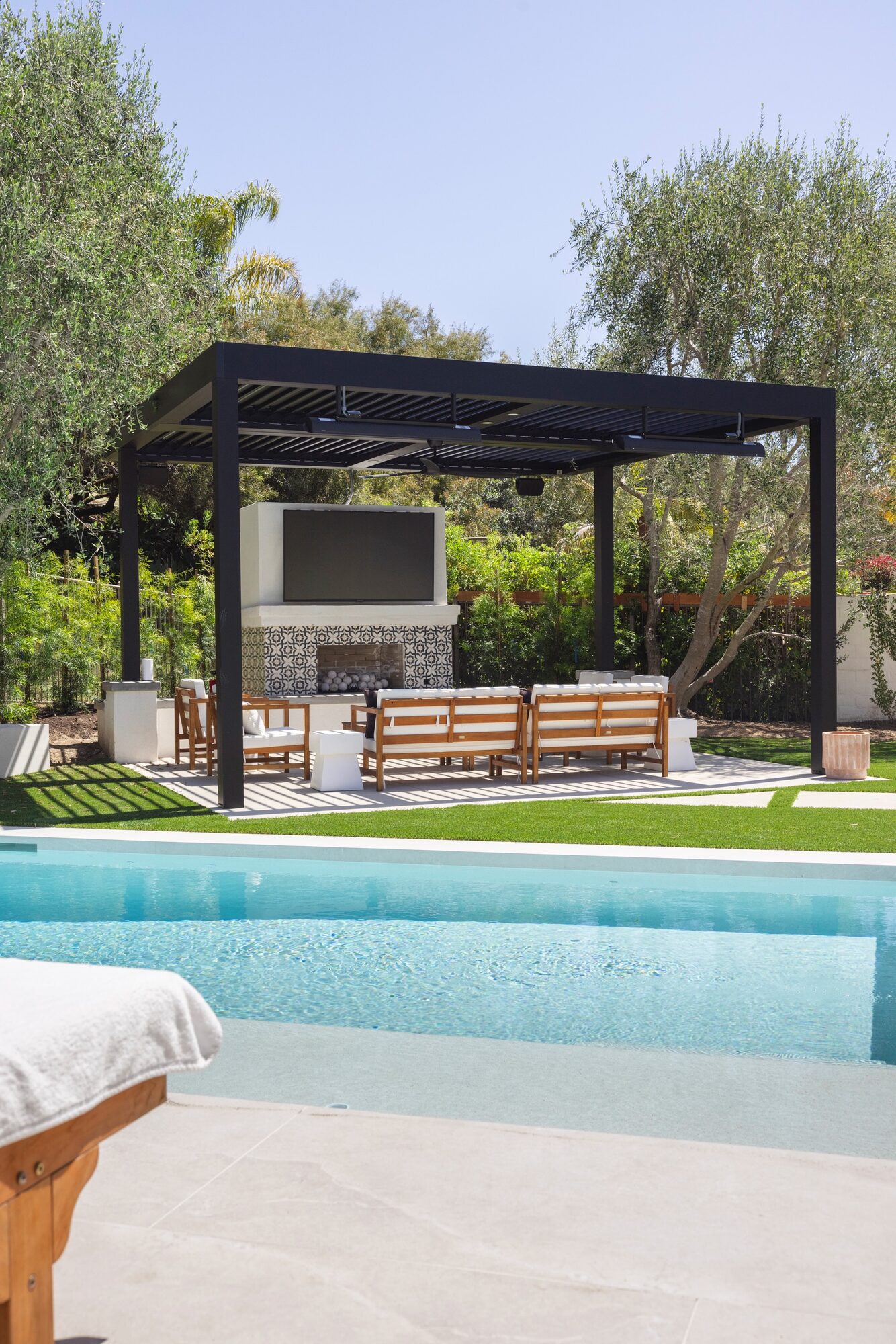 Covered pergola with TV wall, tile fireplace and teak lounge by the pool